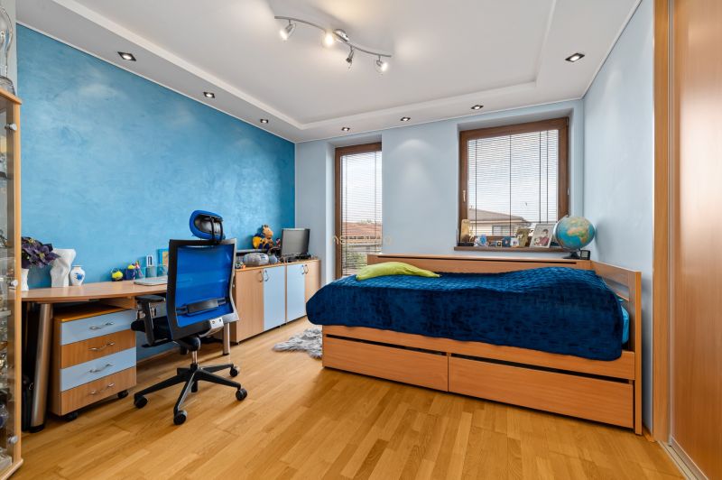 A children's room with a blue wall, a bed, a desk, and a wooden decor floor.