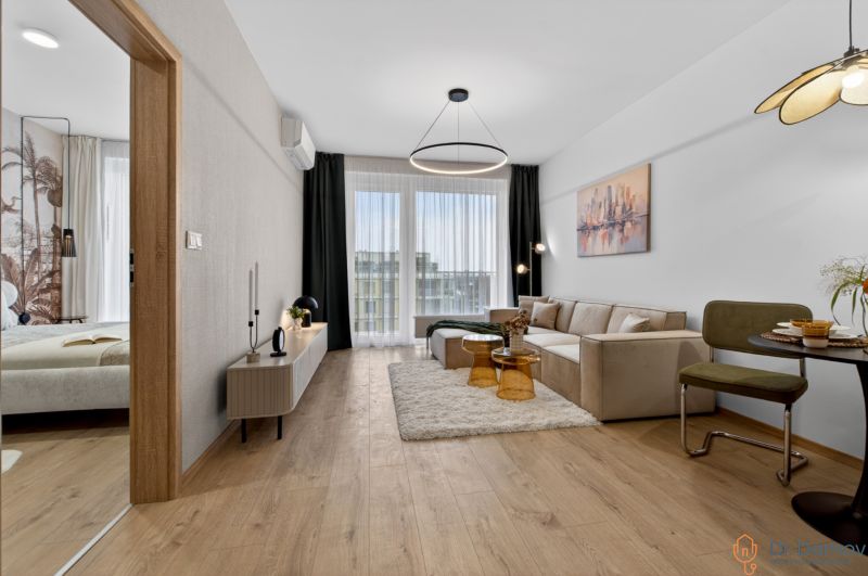 Living room with a sofa, dining area, and wood-patterned flooring in a two-room apartment.