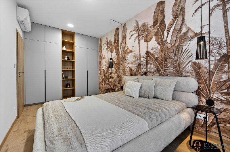 Bedroom in a two-room apartment with a wooden decor floor and wallpaper with an exotic motif.