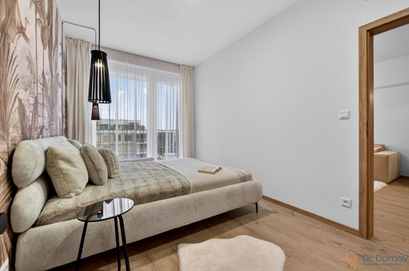 A bedroom with light furniture, a wooden decor floor, a large window, and a curtain.