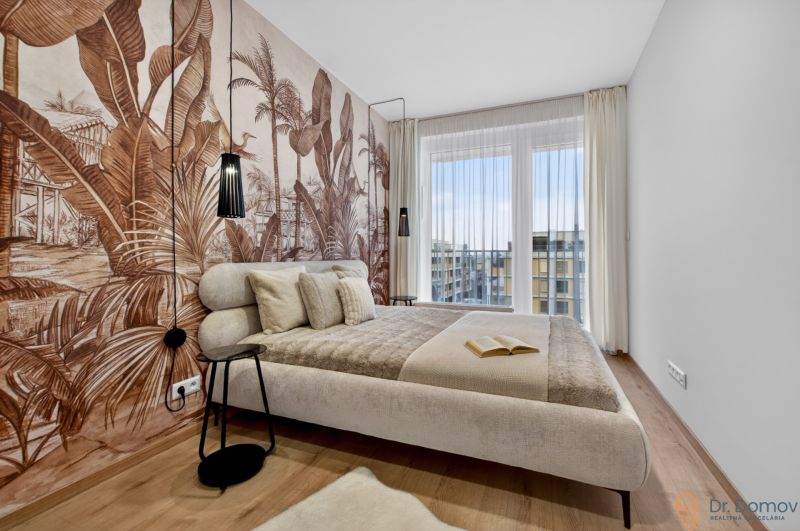 A bedroom in a 2-room apartment with tropical wallpaper and a wooden decor floor.