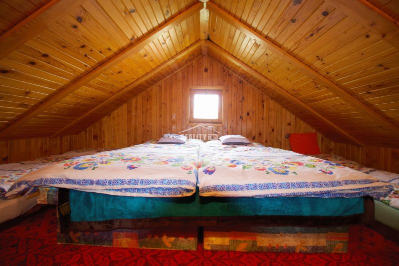 A cottage with wooden paneling has a double bed under a wooden ceiling.