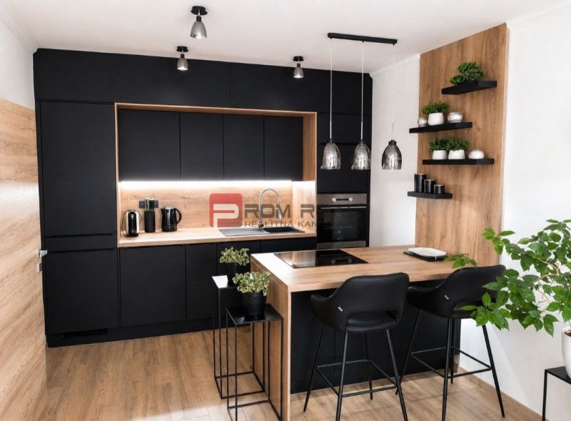 A stylish kitchen with black cabinets and a wooden decor floor in a 2-room apartment.