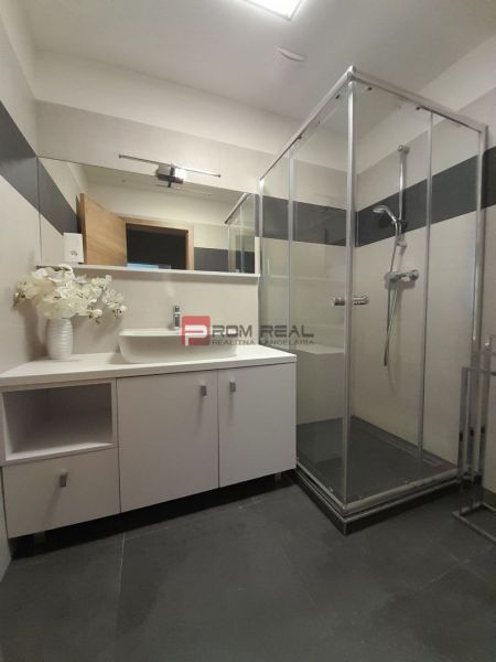 Bathroom in a 2-room apartment with a glass shower enclosure and a large mirror.