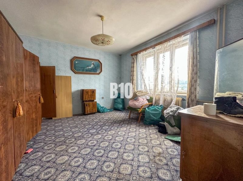 A room in a family house with a carpet, wardrobes, and a chair under the window.