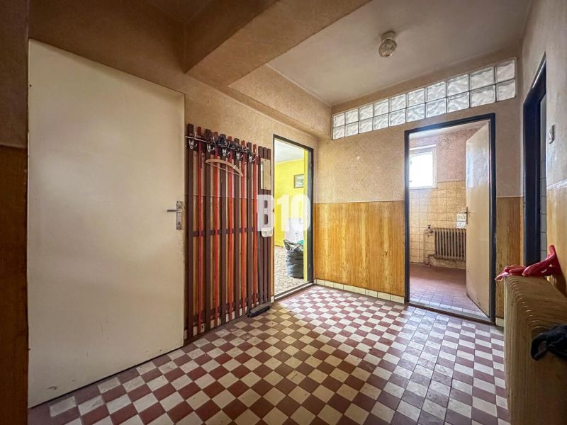 A hallway in a family house with wallpaper, a glass block window, and checkered tiles.