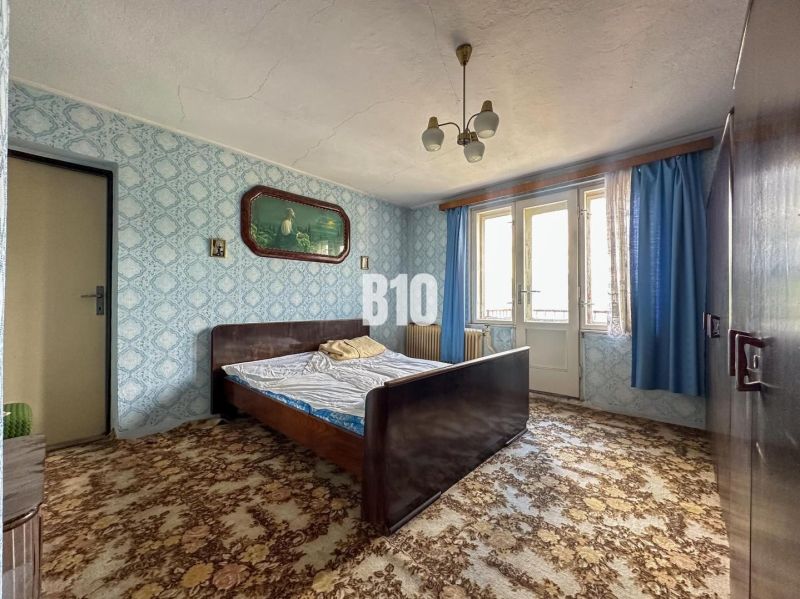 Bedroom in a family house with a patterned carpet and blue curtains.