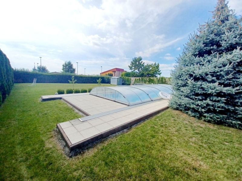 A family house in Nové Zámky with a swimming pool in the garden and a pine tree.