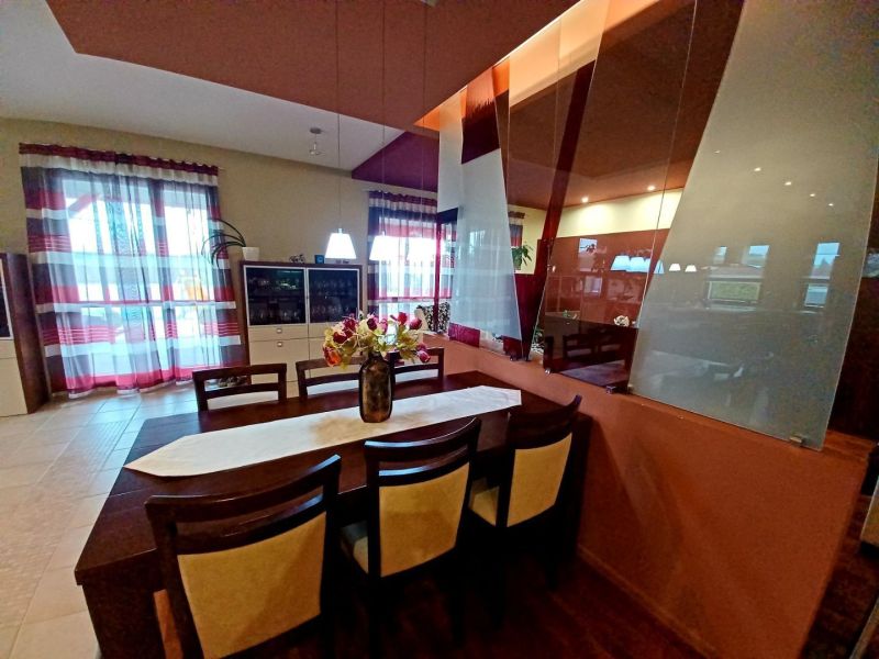 Dining area with flowers, a mirror, and a wooden-patterned floor in a family house.