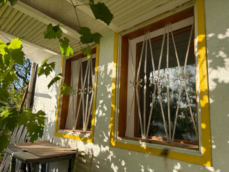 A window with a yellow frame and bars flooded with sunlight in a cottage in Banka.
