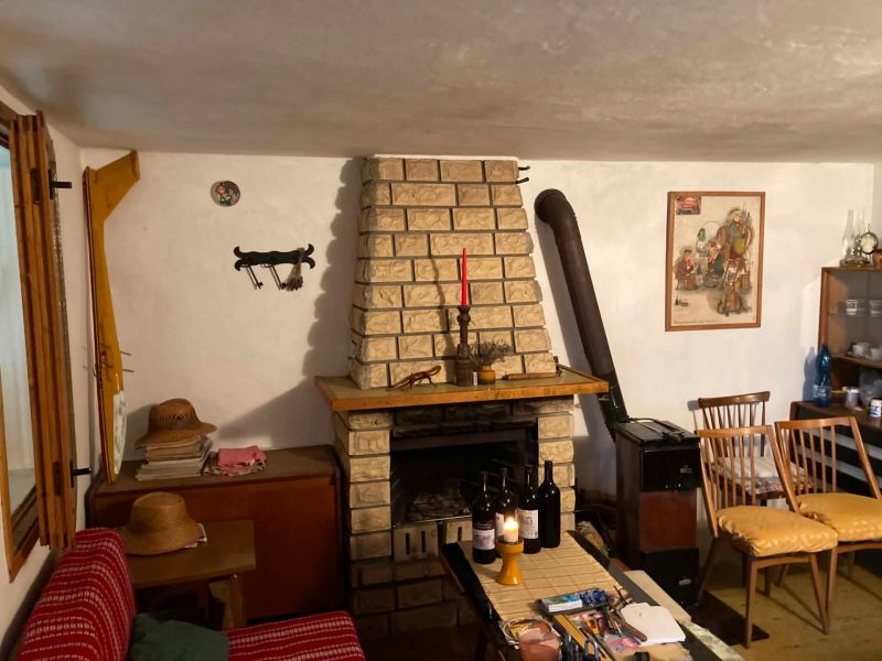 A room in a cottage with a fireplace, wooden chairs, and several bottles of wine on the table.