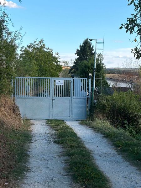 The gate leading to the cottage in Banka surrounded by greenery and a dirt road.