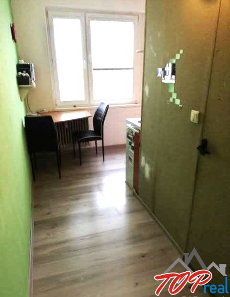 A kitchen in a studio apartment with wooden floor decor and a table by the window.