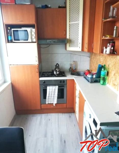 A kitchen in a studio apartment with a wood-patterned floor, basic appliances, and cabinets.