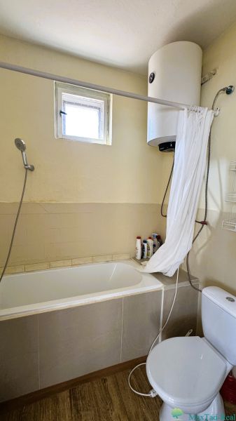 Bathroom with a bathtub, shower, boiler, and wooden decor flooring in a family house.