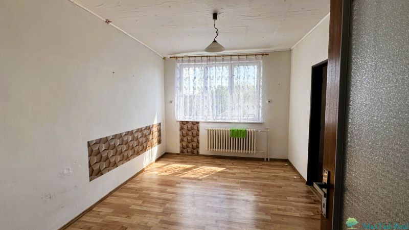 A room in a family house with a wooden decor floor, curtain, and radiator under the window.