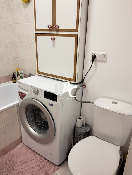 Bathroom in a studio apartment with a washing machine, bathtub, and toilet.