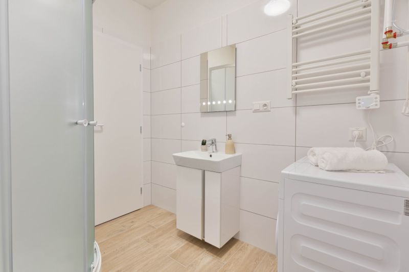 A bathroom in a studio apartment with a wood-patterned floor, white tiles, and a shower corner.