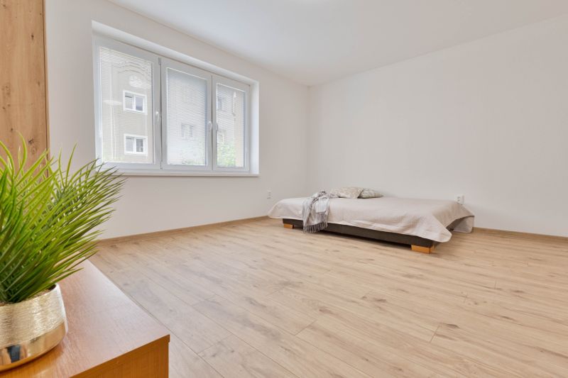 Studio apartment with wood-patterned flooring, a bed, and a large window.