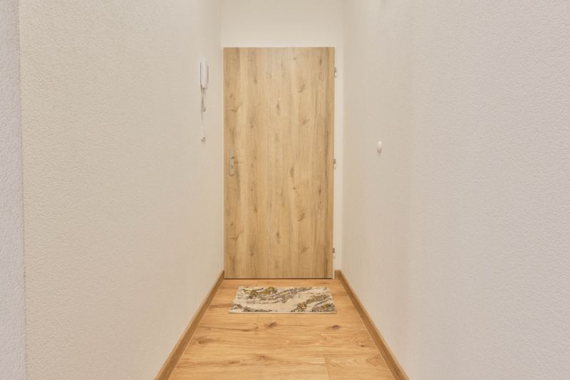 A narrow corridor with white walls and doors with a wooden decor in a studio apartment.