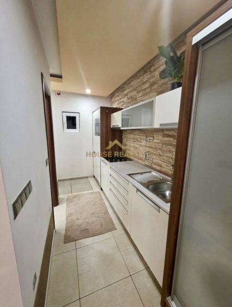 A narrow kitchen in a studio apartment with white cabinets and decorative tiles.