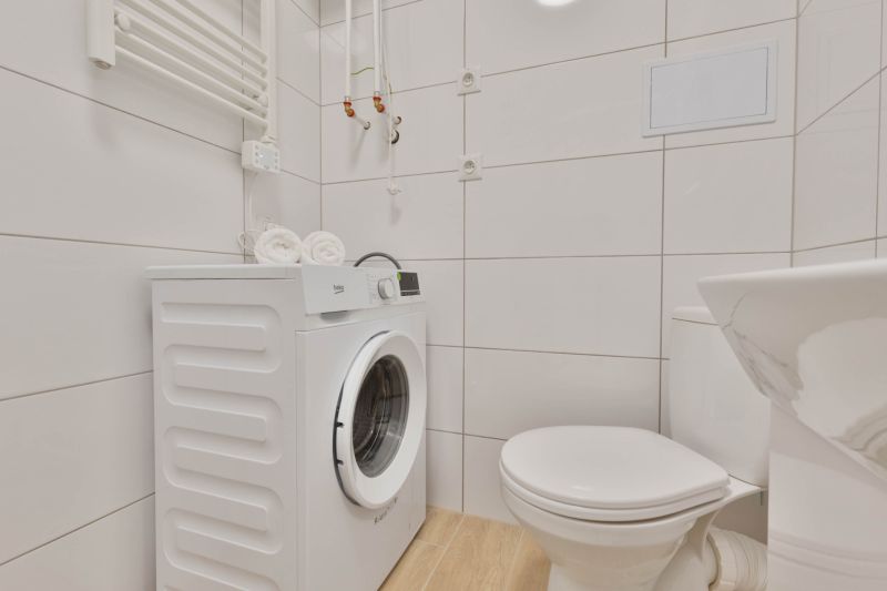 A bathroom in a studio apartment with a washing machine, toilet, and a floor with a wooden decor.