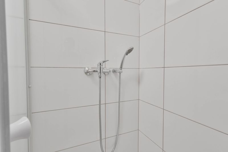 A shower corner with white tiles and a showerhead in a studio apartment.
