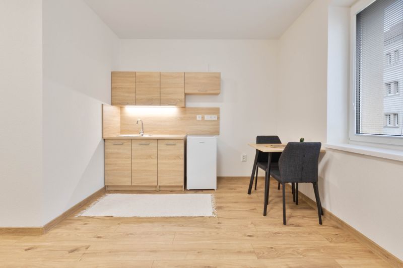 Studio apartment with a kitchenette, refrigerator, and table, complemented by a floor with a wooden decor.