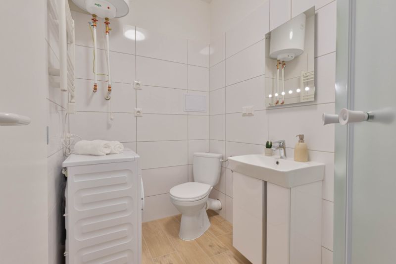 A bathroom in a studio apartment with a washing machine, toilet, sink, and boiler, floor with wooden decor.