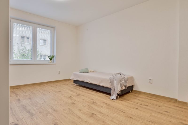 Studio apartment with a bed, wood-patterned floor, and a window with a view.