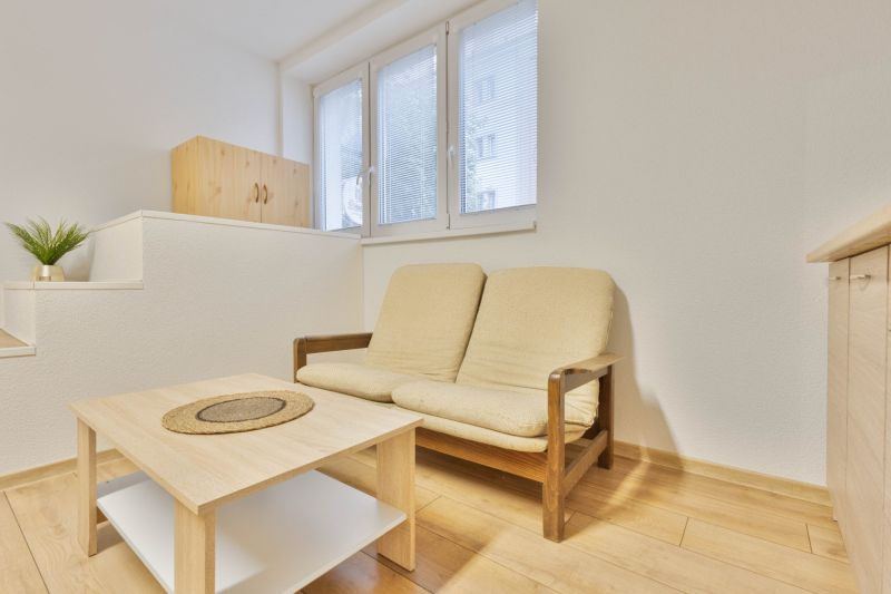 Studio apartment with a sofa, table, and wood-patterned flooring.