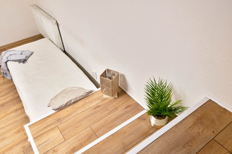 A studio apartment with a wooden floor, a bed, and a potted plant.