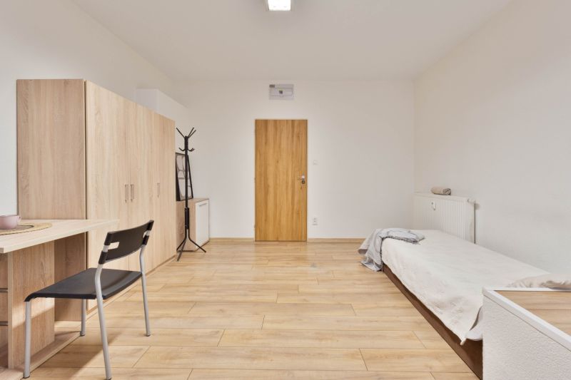 Studio apartment with a bed, wardrobe, table, and floor with wood decor.