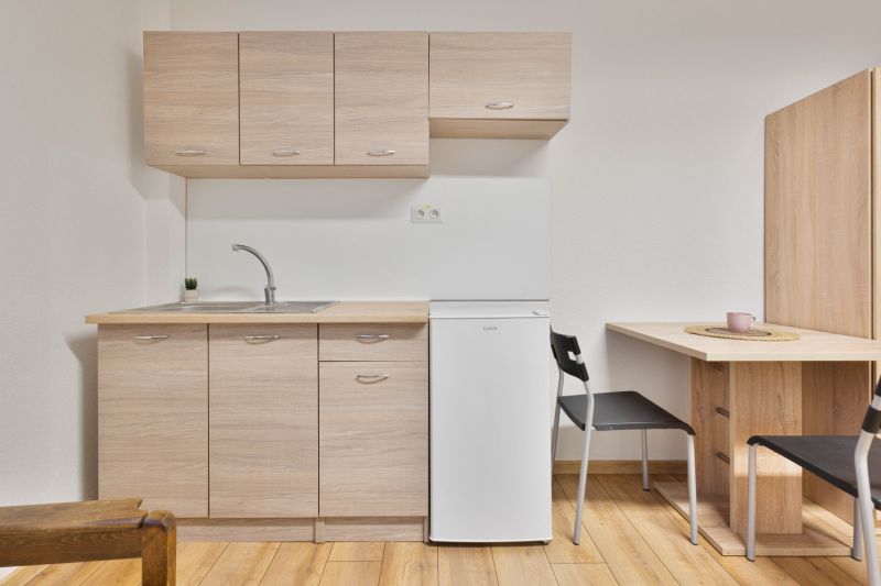 A kitchenette in a studio apartment with a white refrigerator and a wooden decor floor.