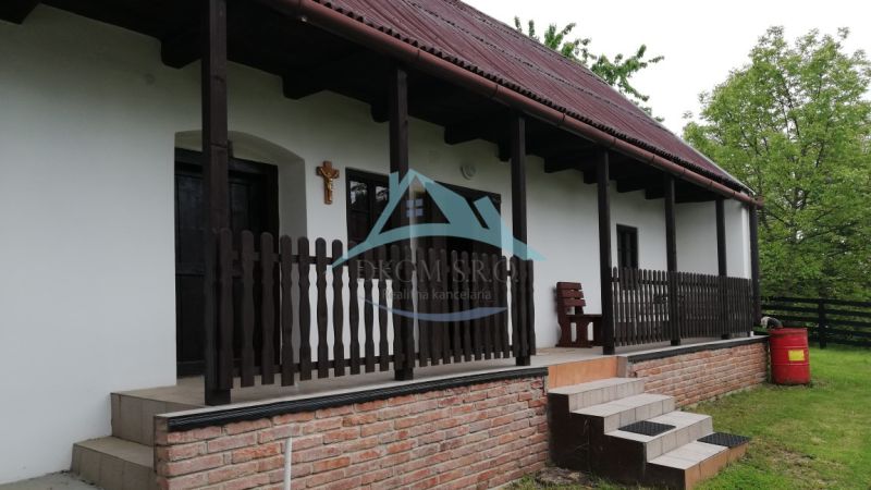 Family house with a terrace, wooden fence, and brick foundation in a natural setting.