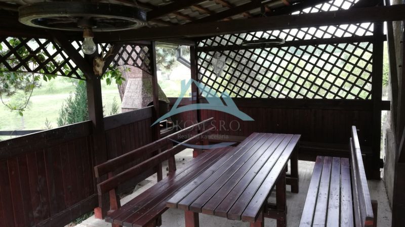 A wooden gazebo with benches located in the garden of a family house.