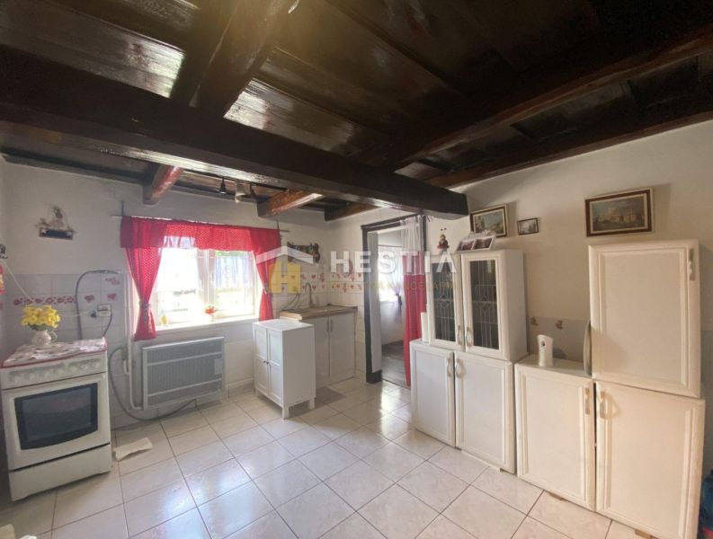 A kitchen in a family house with white cabinets, red curtains, and ceiling beams.