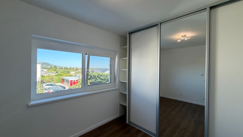 A room with a built-in wardrobe, wood-patterned flooring, a large window with a view.