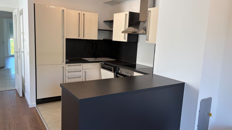 A kitchen in a 3-room apartment with an elegant black countertop and light cabinets.