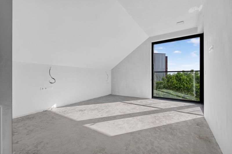 A room with a large window and gray flooring in a multi-room apartment.