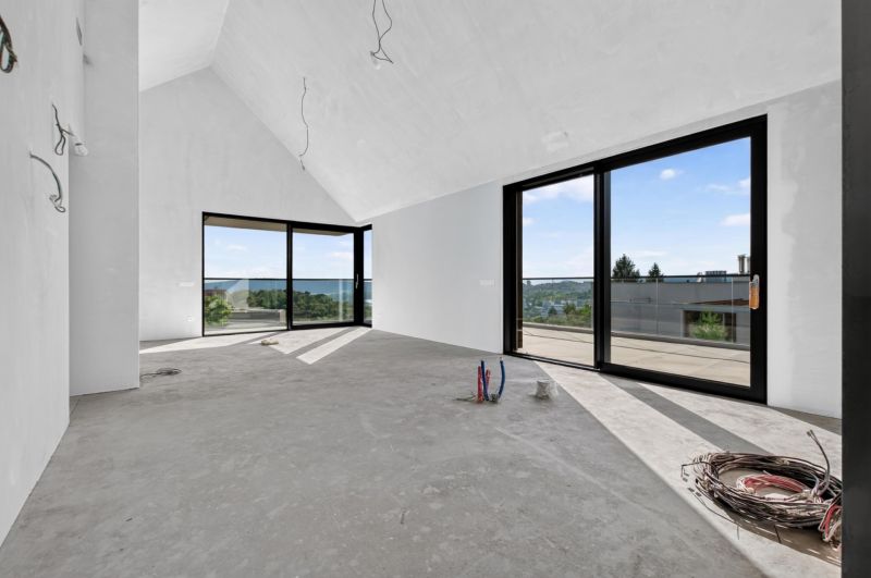 A spacious room in a 5 or more bedroom apartment with large windows and a concrete floor.