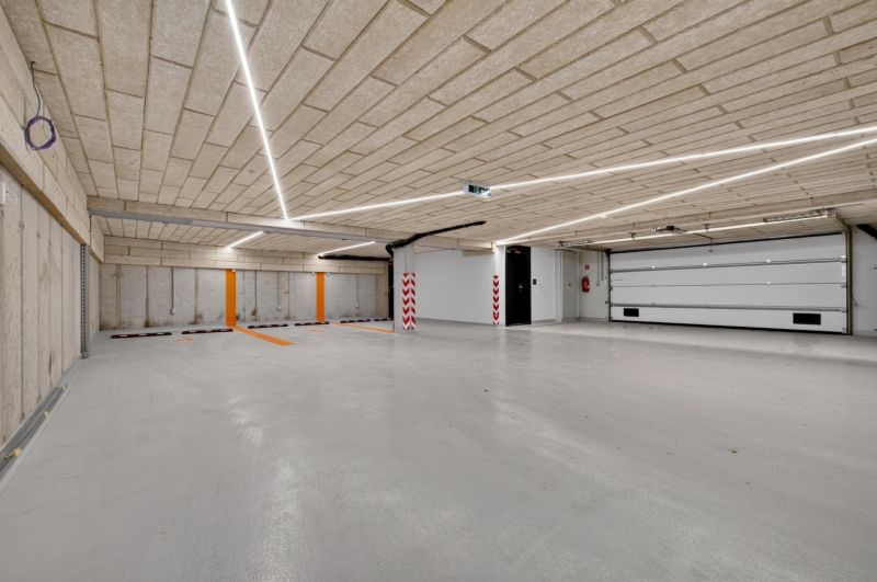 Parking garage with a concrete ceiling and floor, illuminated by linear lights.
