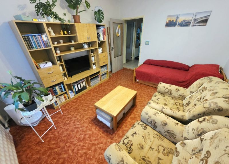 Living room in a 4-room apartment with a sofa, a red seating nook, and a wall shelf.