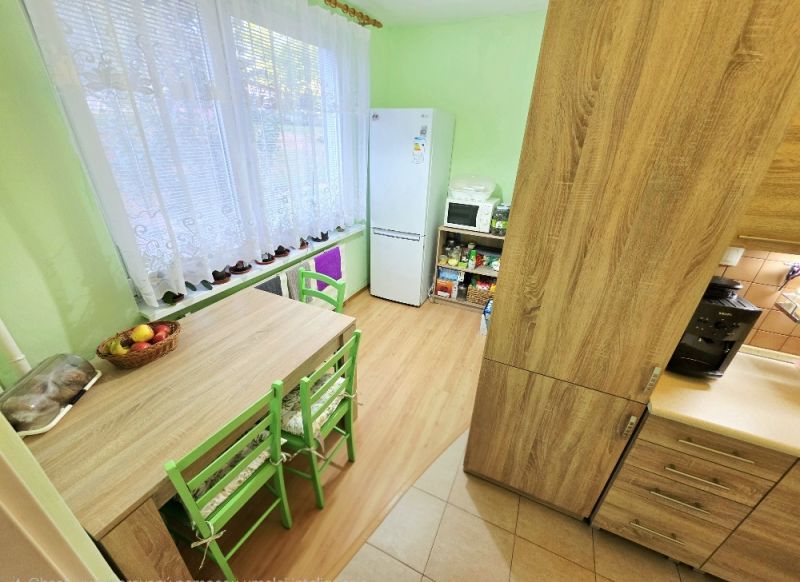 A kitchen in a 4-room apartment with a table, green chairs, and a floor with a wooden decor.