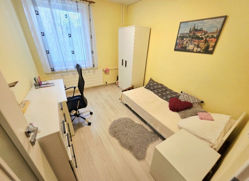 A yellow room with a single bed, a desk, and a wooden-patterned floor in a four-room apartment.