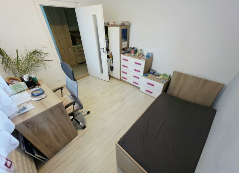 A room in a 4-room apartment with wooden floor decor, a bed, and a desk.