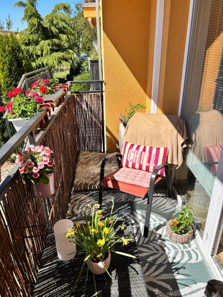 A balcony of a 3-room apartment with comfortable seating, flowers, and a view of greenery.
