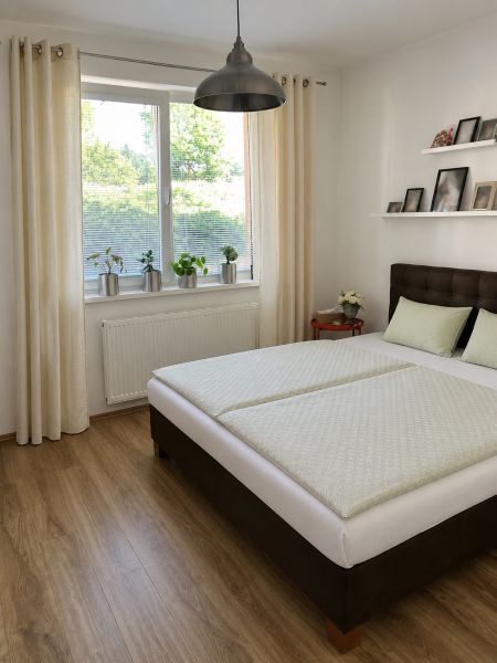 A bedroom with wood-patterned flooring, a large window, and a simple bed in a three-room apartment.