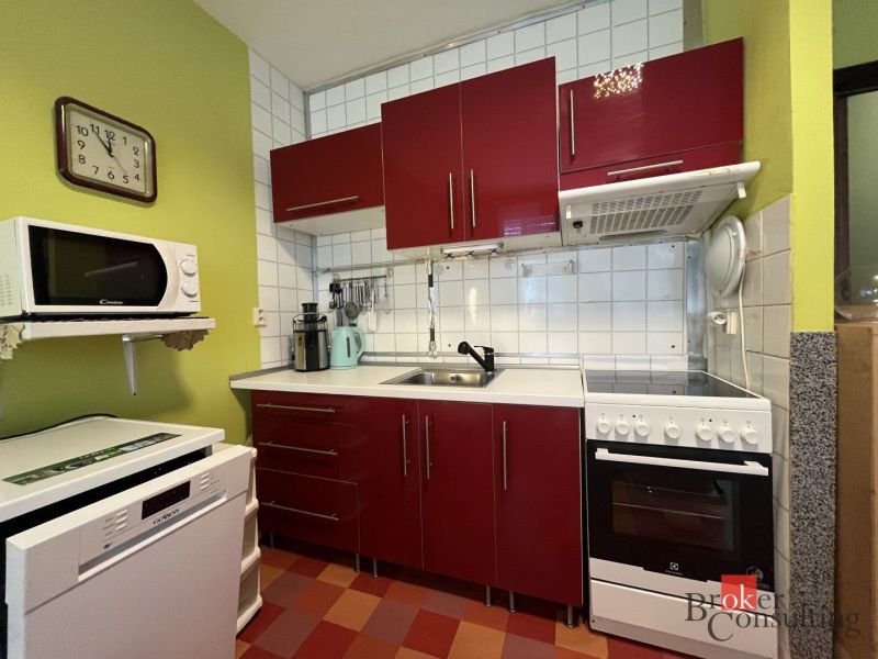 A kitchen in a studio apartment with red cabinets and white appliances.