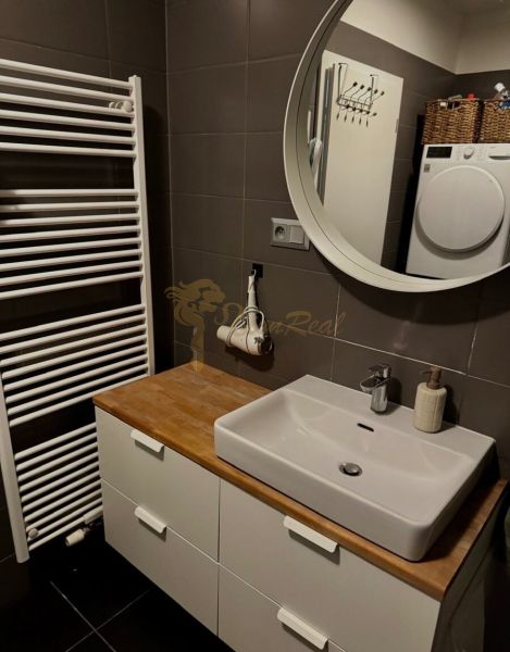 Bathroom with a sink and mirror in a 2-room apartment and a washing machine in the corner.